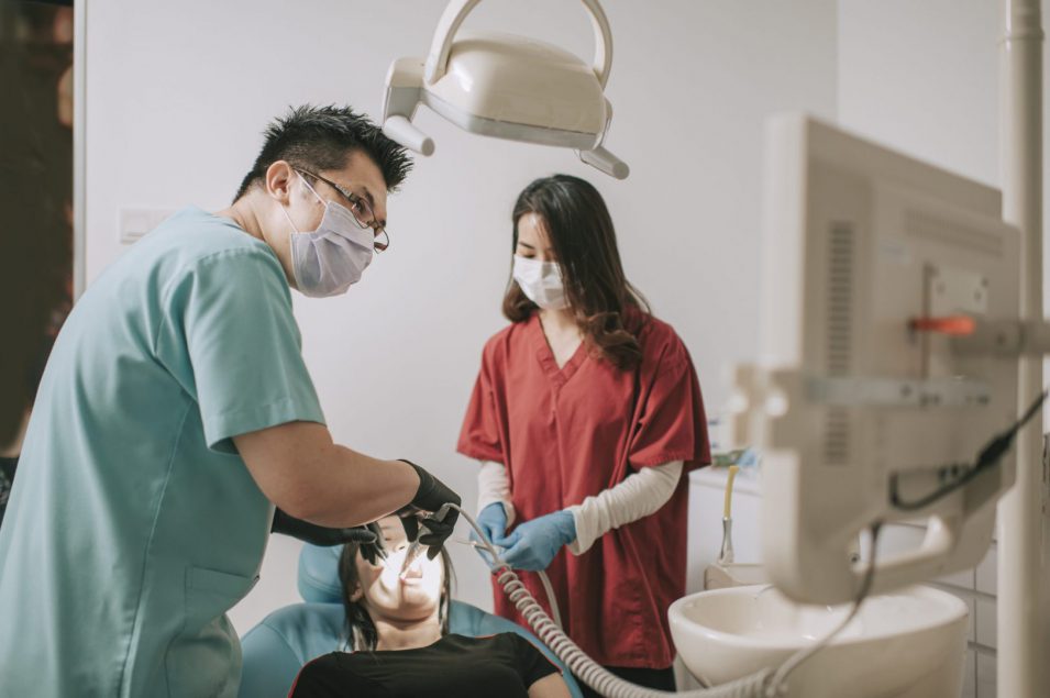 asian chinese dentist perform surgery on his patient with helping from his nurse in clinic