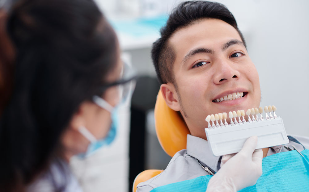 Veneer Shade Selection and Smile Design A dentist using a tooth shade guide to match veneers for a natural-looking smile and consistent colour results